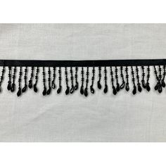 black beaded trim with fringes and beads on white linen background, close up