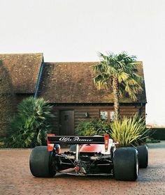 a red and black race car sitting on top of a brick road next to a palm tree