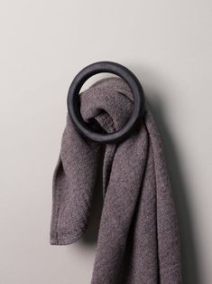 a gray scarf hanging on the wall with a black ring at the end of it