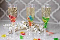 three champagne flutes filled with gummy bears and candy on a table next to confetti