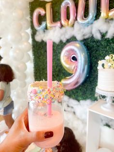 a person holding up a drink in front of balloons