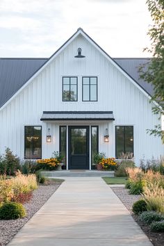 a white house with lots of windows and plants around it's front door, along with a walkway leading to the front door