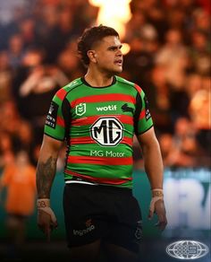 a rugby player in green and red jersey walking on the field with fans behind him