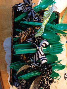 a box filled with lots of green and black plastic utensils sitting on top of a wooden table