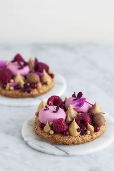 two small desserts with fruit on them are sitting on plates, one is topped with nuts and the other has raspberries