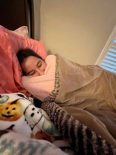 a woman laying in bed with her eyes closed and covered by a pink blanket over her head