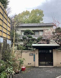 a house with trees and bushes in front of it, next to a parking lot