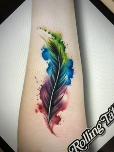 a watercolor feather tattoo on the arm and leg with blue, green and purple ink