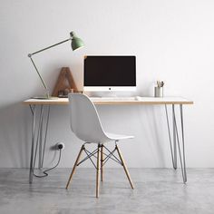 a desk with a computer on it next to a white chair and a green lamp