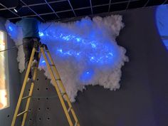 a man standing on a ladder in front of a blue light and clouds hanging from the ceiling