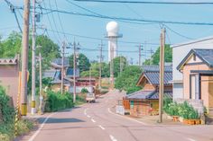 an empty street with houses and power lines in the foreground, and a water tower in the background