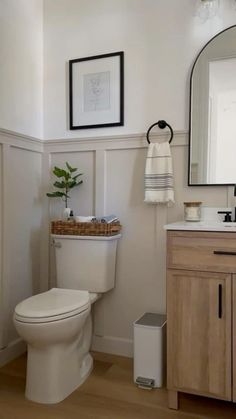 a white toilet sitting in a bathroom next to a wooden cabinet and sink with a mirror above it