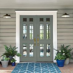 a front door with two potted plants on the side and a blue rug in front