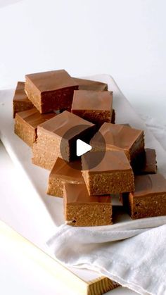 several pieces of brownie on a white plate with a cloth next to it and a book in the background