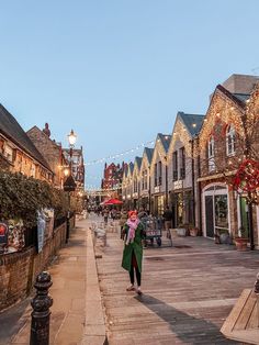 a woman walking down a street in front of buildings with christmas lights on the side