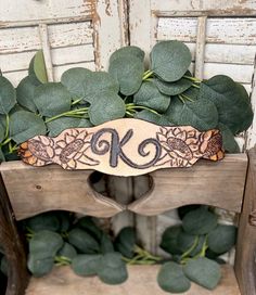 a wooden sign with the letter k on it sitting in front of some green leaves