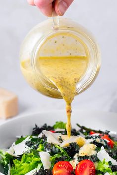 someone pouring dressing over a salad in a white bowl with tomatoes and lettuce