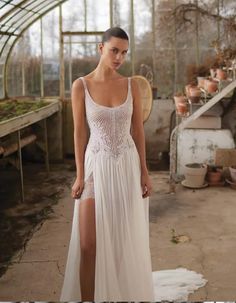 a woman wearing a white dress with a slit in the side and an open - air greenhouse behind her