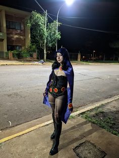 a woman dressed in costume walking down the street at night with her hands on her hips