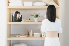 a woman standing in front of a shelf filled with white towels and other bathroom items