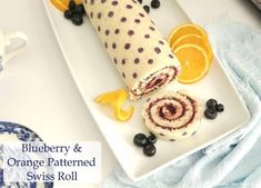 blueberry and orange patterned swiss roll on a white plate with lemons, blueberries, and an orange slice