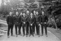 a group of men standing next to each other in front of some bushes and trees