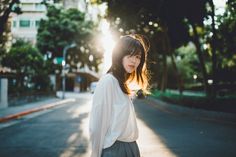 a woman standing on the side of a road with trees in the background and sunlight shining through her hair