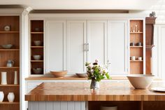 a kitchen with white cabinets and wooden counter tops, along with a vase filled with flowers