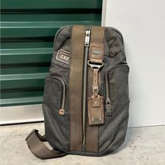 a gray backpack sitting on the ground next to a green garage door, with one zipper open