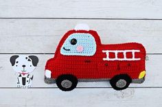 a crocheted red truck with a black and white dog next to it on a wooden surface