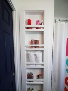 a bathroom with white shelves filled with toilet paper and other items on the shelf in front of the door