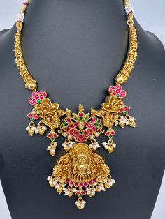 Jadau Kundan Goddess Lakshmi Kanti Necklace with matching JhumkasColor : GoldenSize : Necklae Length : 16 Inches; Earrings Length : .2.5 Inches approxStones : Red Green Jadau Kundan Pearls