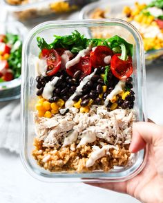 a person holding up a plastic container filled with rice, beans and veggies