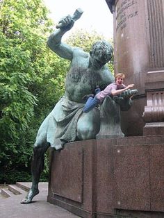 a statue of a man holding a child in front of a monument with trees behind it