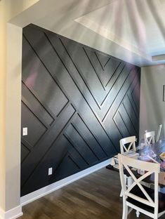 a dining room table and chairs in front of a black wall with geometric designs on it