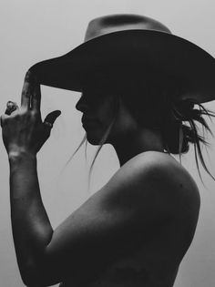 a woman wearing a large hat and holding her hand up to her face while standing in front of a white wall