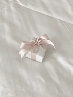 a white gift box with a pink bow on it sitting on top of a bed