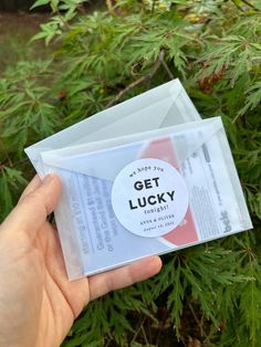 someone is holding up an envelope with the word get lucky printed on it in front of some plants