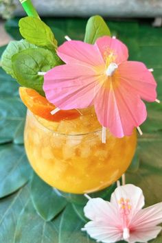 there is a drink with flowers in it on the table next to some leaves and flowers