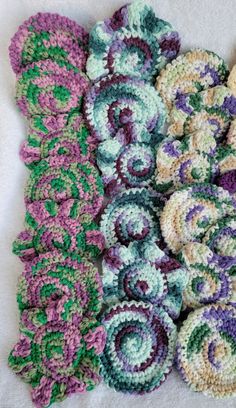 several crocheted pieces of yarn laid out on a white surface, one with green and purple flowers