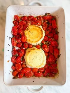 two eggs on top of tomatoes in a white dish