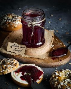 a jar of jam sitting on top of a wooden cutting board next to bagels