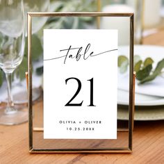 a table number is displayed in a frame on top of a wooden table with plates and silverware