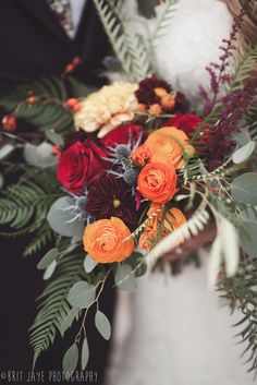 the bride and groom are holding their bouquets with red, orange flowers on them