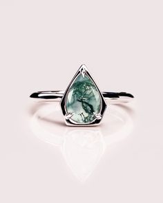 a white gold ring with a green stone in the shape of a tear shaped triangle