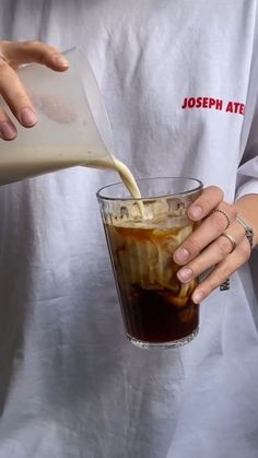 a person pouring something into a glass filled with ice and liquid from a pitcher in their hand