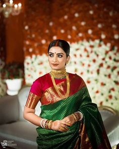 a woman in a green and red sari with gold jewelry on her neck, standing next to a couch