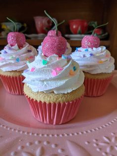 three cupcakes with white frosting and strawberries on top are sitting on a pink plate