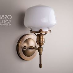 a wall light with a white glass shade on it's arm and a brass finish