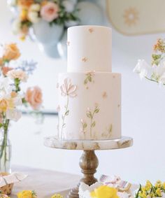 a white cake with flowers on it sitting on a table next to vases filled with flowers